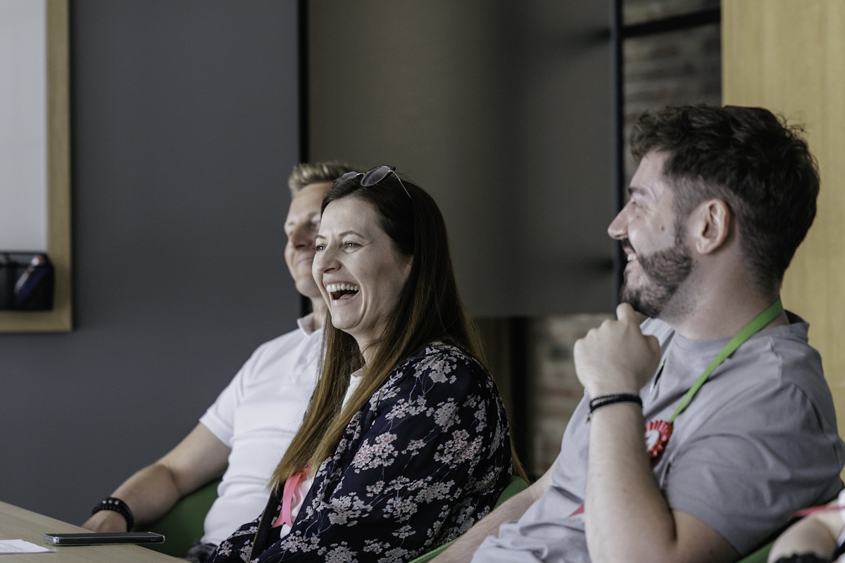 Three members of the Leroy Merlin team sit in a conference room and laugh during a meeting. A visible woman with a pin of the “Change perspective” campaign